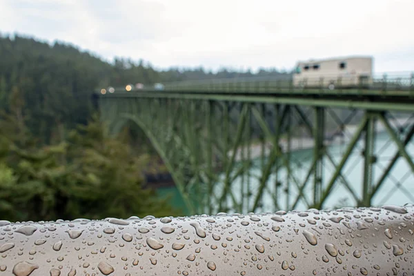 Corrimão coberto de gotas de água na frente de uma ponte verde — Fotografia de Stock