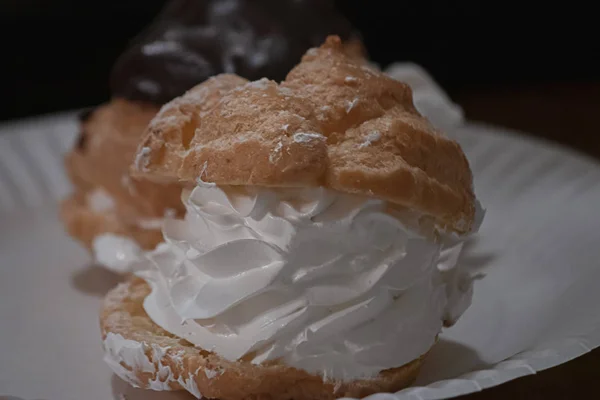 Bouffées de sucre et de crème glacée au chocolat brillante remplies d'un tourbillon de crème fouettée blanche sur des assiettes en papier — Photo