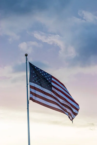 Amerikanska flaggan flyger högt i molnigt himmel under våren mot solnedgången — Stockfoto