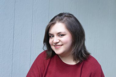 Kırmızı elbiseli genç kadın mavi eve karşı gülümsüyor.