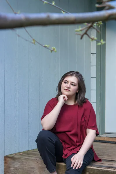 girl with hand under chin stares off into distance on porch