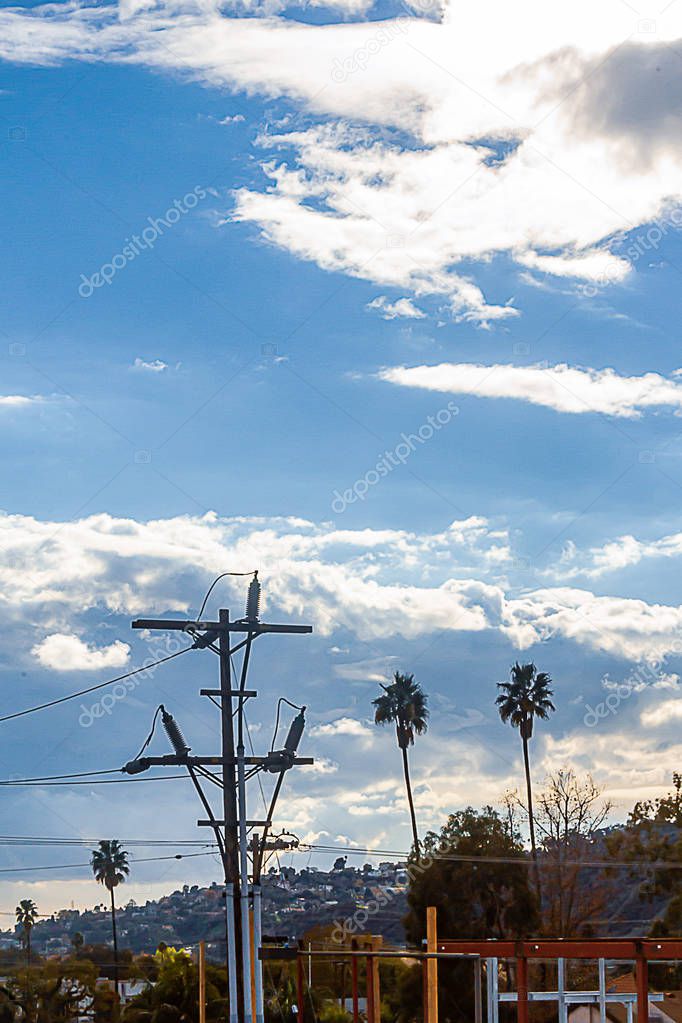 powerline and pole with palm trees and construction, against hillside