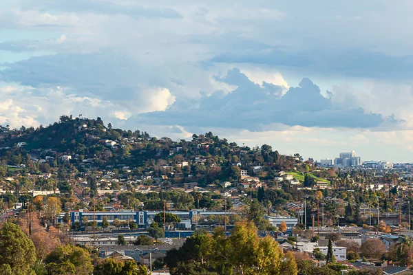 Stadslandschap met groenblijvende en disiduous bomen met heuvels en bewolkte blauwe hemel en heuvel huizen — Stockfoto