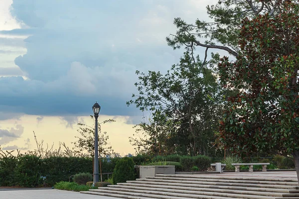 Pouliční lampa na kopci se schodištěm, lavičkou zeleně a velkými mraky — Stock fotografie