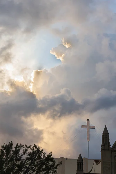 Cruz en el edificio con torres y árboles contra grandes nubes de colores — Foto de Stock