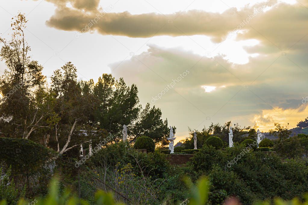grecian female statues in a hillside garden with greenery, overlooking panaramic cloudscape,