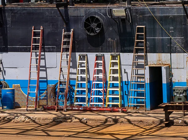 Шесть лестниц, прислонившихся к борту корабля в гавани — стоковое фото