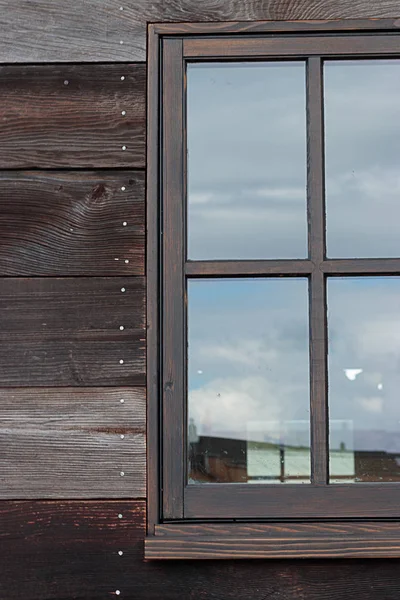 Großes Fenster auf einem Holzgebäude, das den Himmel an einem bewölkten Tag reflektiert — Stockfoto