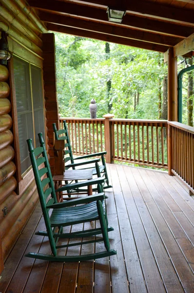 Two rocking chairs and a swing on a wooden wrap around deck — 스톡 사진