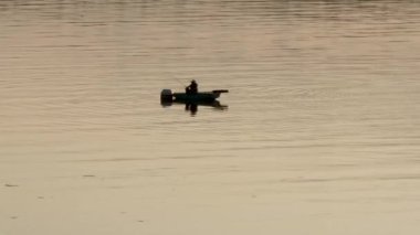 Gün batımında teknede balık tutan kişi.