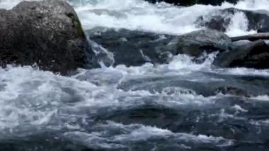 Nehirdeki büyük kayaların üzerinden akan suyun detaylı görüntüsü