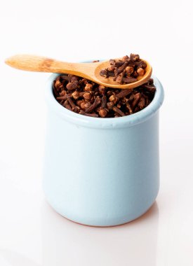 Çamur tenceresinde baharatlı karanfil, beyaz bir arka planda izole edilmiş tahta bir kaşık.