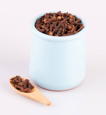 Çamur tenceresinde baharatlı karanfil, beyaz bir arka planda izole edilmiş tahta bir kaşık.