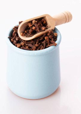 Çamur tenceresinde baharatlı karanfil, beyaz bir arka planda izole edilmiş tahta bir kaşık.