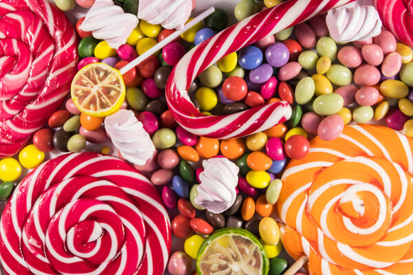 Background of colorful chocolate candies, lollipops, candy cane and marshmallows