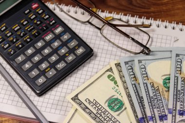 Defter ile dolar, kalem, gözlük ve ahşap masa hesap makinesi. Mali kavramı. İş rapor
