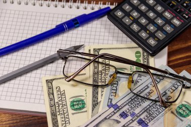 Defter ile dolar, kalem, gözlük ve ahşap masa hesap makinesi. Mali kavramı. İş rapor