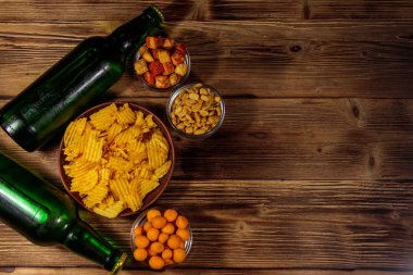 Bira şişeleri ve ahşap masada bira için çeşitli atıştırmalıklar. Üst görünüm, alanı kopyala