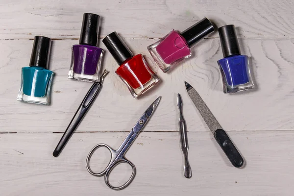 Basic set of manicure tools on white wooden background. Nail and cuticle scissors, cuticle trimmer, nail file and nail polish bottles on wood table