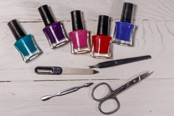 Beyaz ahşap arka planda temel manikür aletleri seti. Tırnak makası, tırnak makası, tırnak törpüsü ve oje şişeleri.