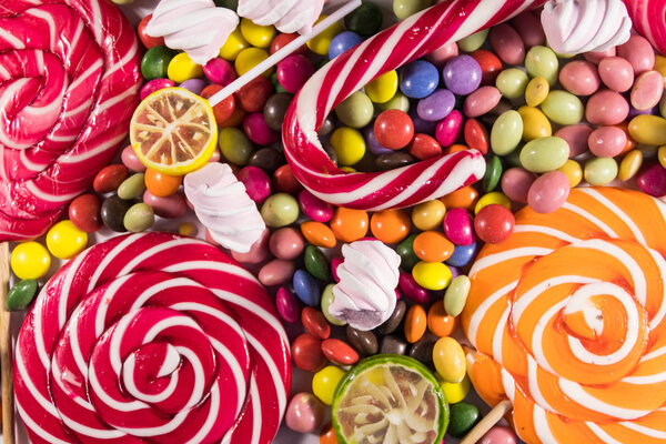 Background of colorful chocolate candies, lollipops, candy cane and marshmallows