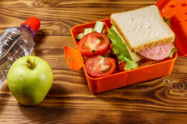 Okul öğle yemeği kutusu sandviç ve taze sebze, şişe su ve yeşil elma ahşap masa üzerinde. Sağlıklı beslenme kavramı