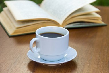 Bir fincan kahve ve kitap ahşap masada.