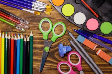 Okul kırtasiye malzemeleri kümesi. Renkli kalemler, suluboya boya, boya fırçaları, kalem, makas, silgi, kalemtıraş ahşap masa üzerinde. Geri okul kavramı