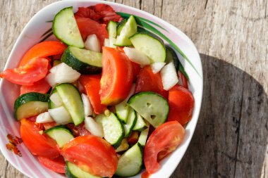 Domates, salatalık, soğan ve zeytin yağı ahşap masa üzerinde taze sebze salatası. Üstten görünüm