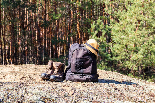 Tourist backpack, hiking boots and hat on the glade in pine forest. Hike concept