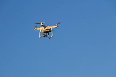Mavi gökyüzünde süzülen kameralı bir kuadkopter.