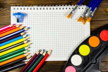 Ahşap arka plan üzerinde çizim araçları kümesi. Defter, suluboya boya, Boya fırçaları, boş renk masada kalemleri