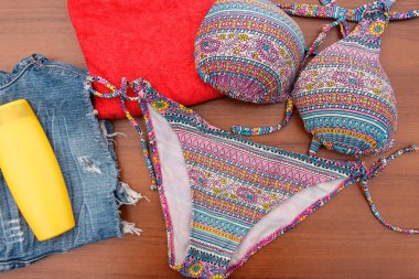 Ahşap arka plan üzerinde beachwear kümesi. Güneş kremi, havlu, mayo ve jean şort. Yaz tatil kavramı