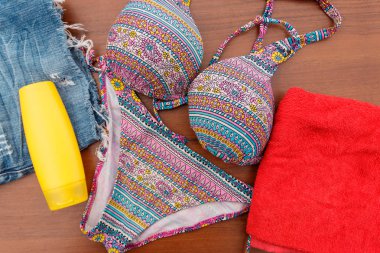 Ahşap arka plan üzerinde beachwear kümesi. Güneş kremi, havlu, mayo ve jean şort. Yaz tatil kavramı