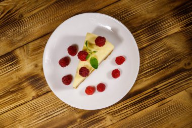 Tahta masadaki beyaz tabakta ahududu bulunan lezzetli New York peynirli keki. Üst görünüm