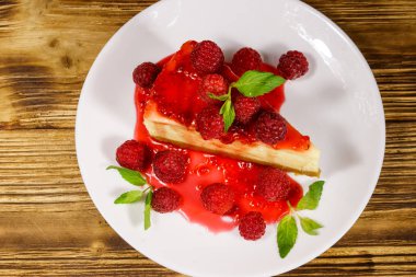 Ahududu ve ahududu reçelli lezzetli New York peynirli keki ahşap masada beyaz bir tabakta.