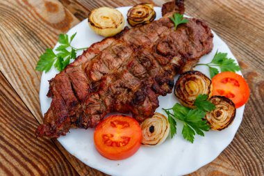 Izgara domuz etli soğan, domates ve maydanoz ahşap masa üzerinde beyaz plaka