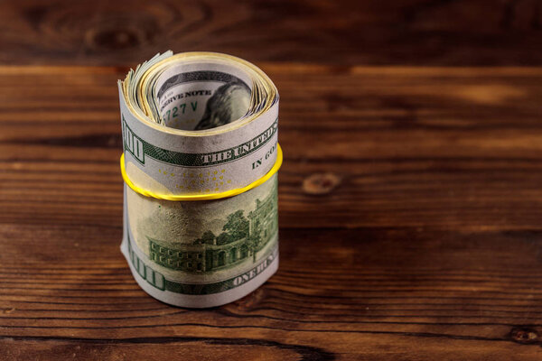 Рулон стодолларовых купюр на деревянном столе
