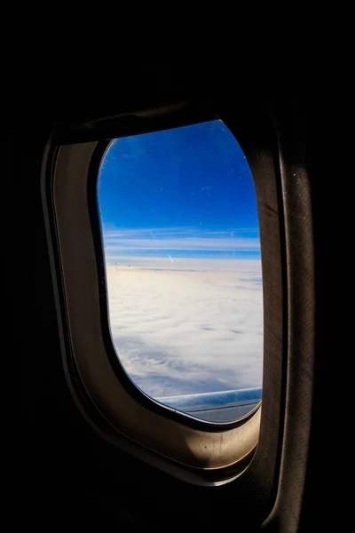 Uitzicht op blauwe lucht met witte wolken door de patrijspoort venster vliegend vliegtuig — Stockfoto