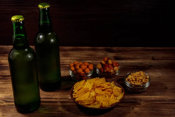 Láhve piva a různé občerstvení na dřevěný stůl — Stock fotografie