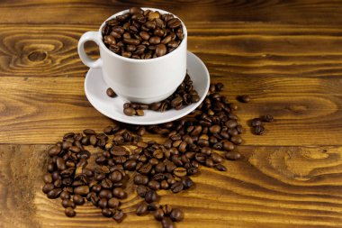 Ahşap masa üzerinde beyaz fincan kahve çekirdekleri