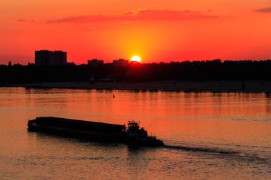 Römorkör, gün batımında Dinyeper nehrinde ağır, uzun bir mavnayı itiyor.
