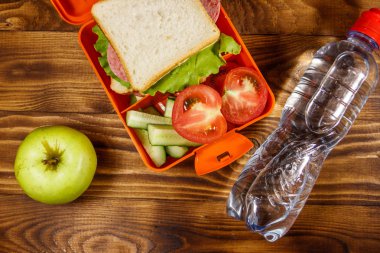 Okul öğle yemeği kutusu sandviç ve taze sebze, şişe su ve yeşil elma ahşap masa üzerinde. Sağlıklı beslenme kavramı. 
