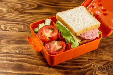 Sandviç ve ahşap masa üzerinde taze sebze okul öğle yemeği kutusu
