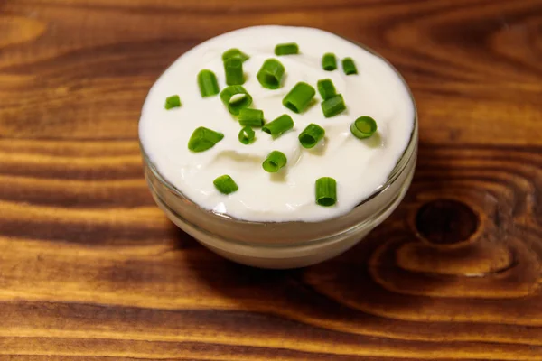 Sour cream with green onion in glass bowl on wooden table — Stock Photo, Image