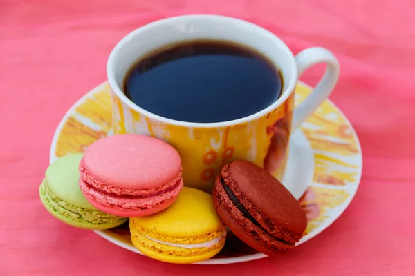 गुलाबी पृष्ठभूमि पर स्वादिष्ट रंगीन मैकरॉन के साथ कॉफी का कप — स्टॉक फ़ोटो, इमेज