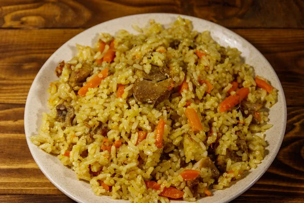 Pilaf with meat, rice, carrot and onion in a plate on wooden table