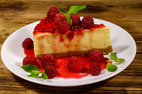 Piece of tasty New York cheesecake with raspberries and raspberry jam in a white plate on wooden table — Stock Photo, Image