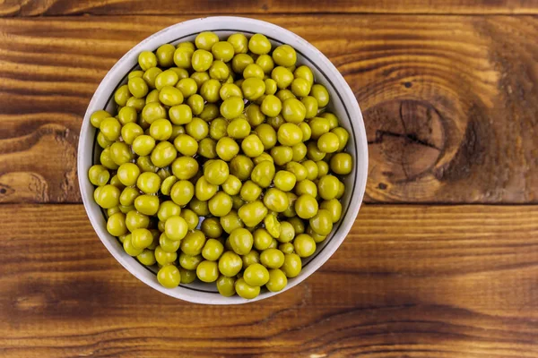 Bowl with canned green peas  on wooden table. Top view — Stock Photo, Image