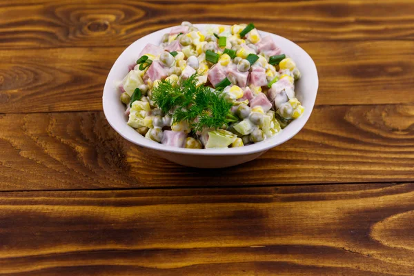 Salată gustoasă cu cârnați, mazăre verde, conserve de porumb, ardei gras, castravete și maioneză pe masă de lemn — Fotografie, imagine de stoc
